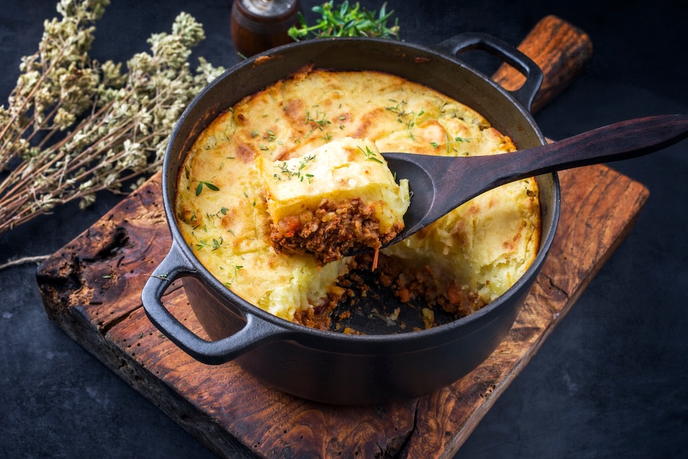 Traditional English shepherd pie offered as closeup in a Dutch oven on a wooden board