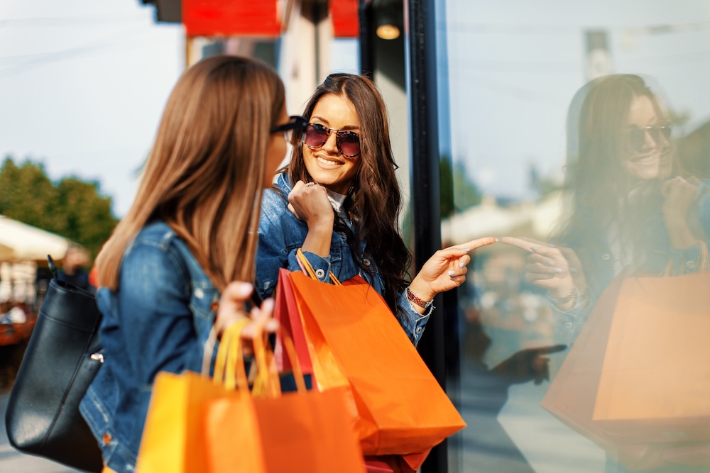 Two young women in shopping looking at shop window in the city.